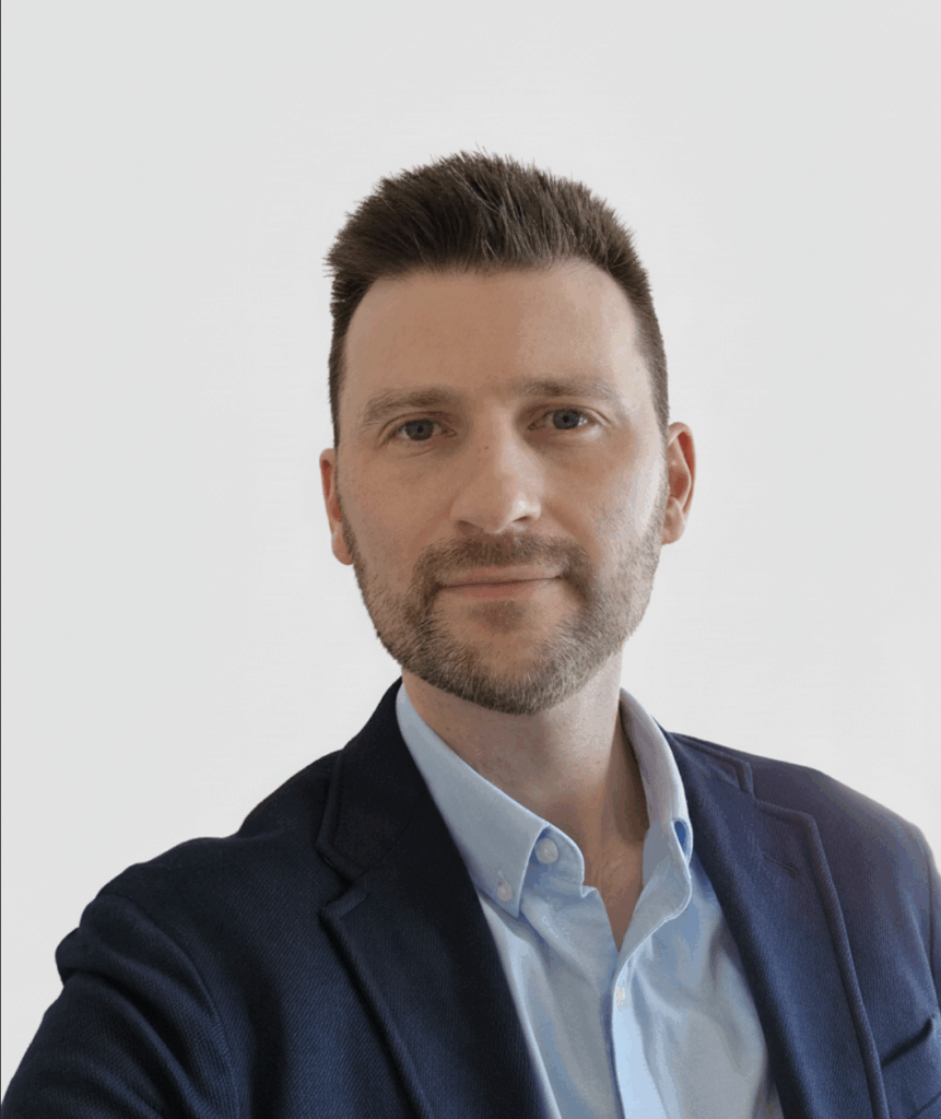 A head-and-shoulders portrait of Nathan Windle. Nathan is a middle-aged white man, with short dark hair and a close-cut beard and moustache. He is smiling at the camera.